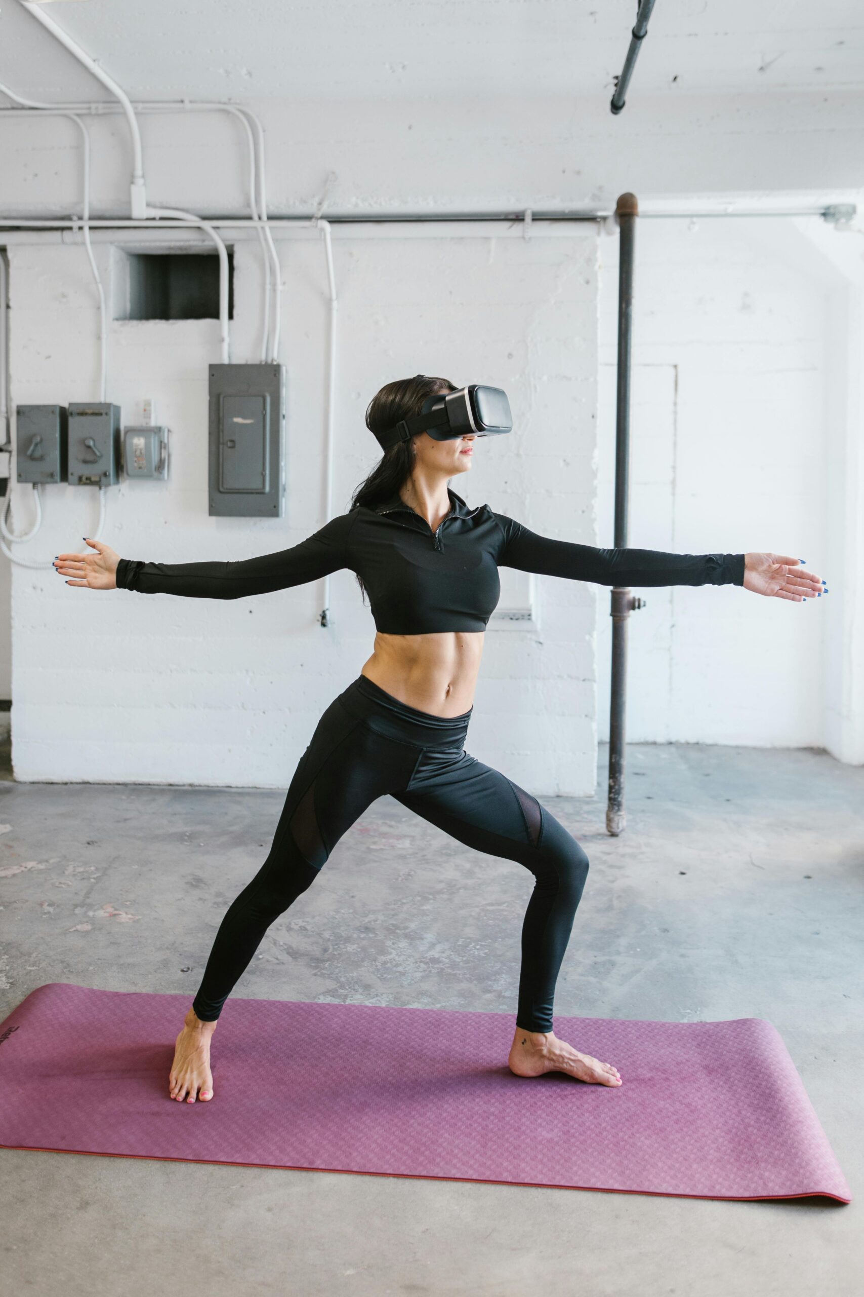 Woman in athletic wear doing yoga with VR goggles on a mat indoors.